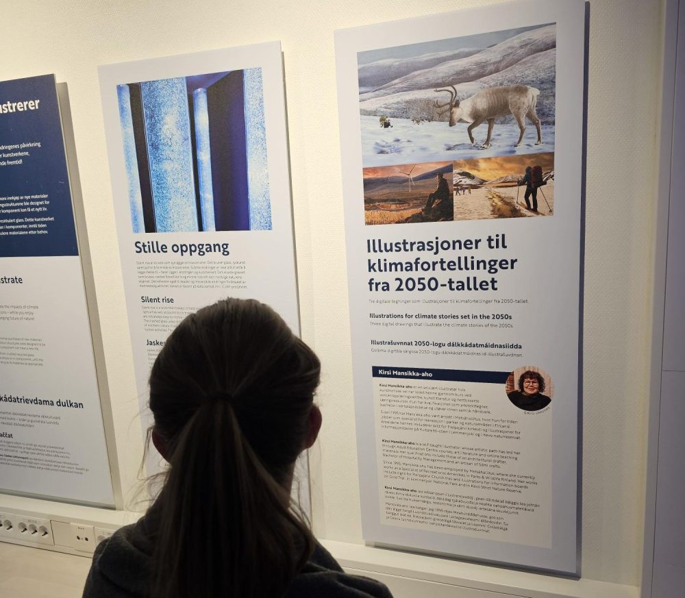 En person står foran en vegg og leser en informasjonsplakat i en utstilling. Plakaten har overskriften «Illustrasjoner til klimafortellinger fra 2050-tallet» og inneholder tekst på flere språk samt bilder, blant annet av en rein i et vinterlandskap og personer i naturen. Ved siden av henger en annen plakat med overskriften «Stille oppgang» og tilhørende bilde av en installasjon med lysende rør. Veggen er hvit og godt opplyst, med flere utstillingsplakater plassert ved siden av hverandre.